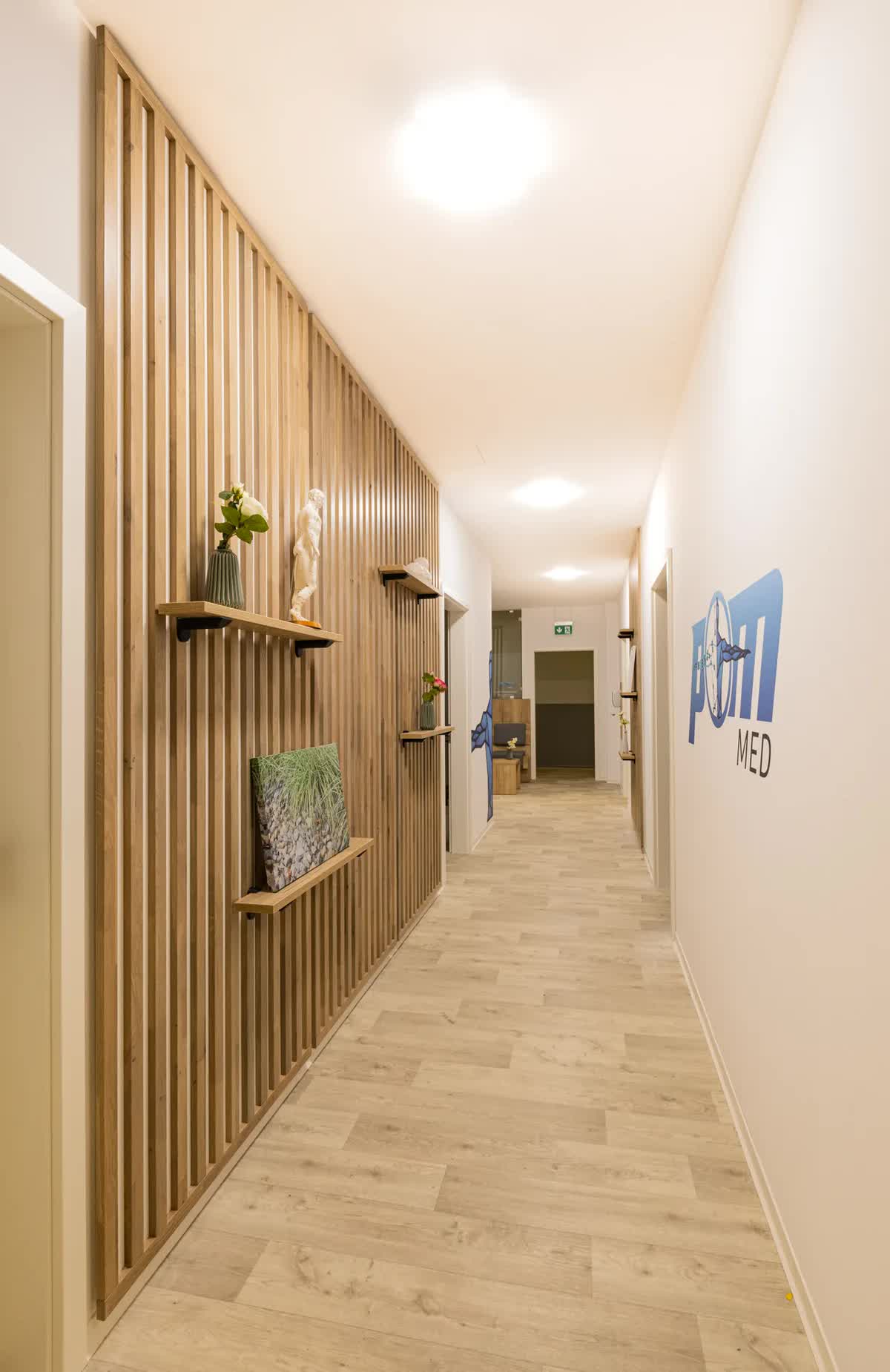 Flur der Praxis POM MED mit Holzlamellen, Regalen und dem POM-MED-Logo an der Wand