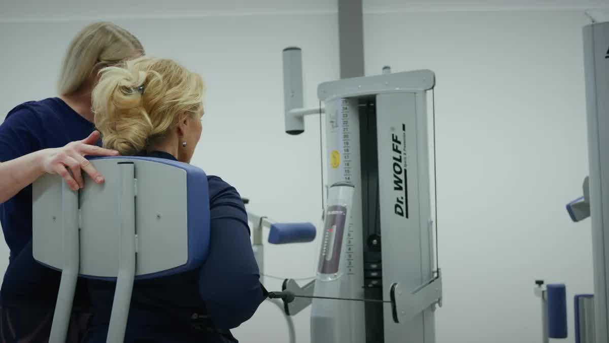 Patientin trainiert am Dr. Wolff Therapiegerät, eine Therapeutin der POM MED begleitet sie