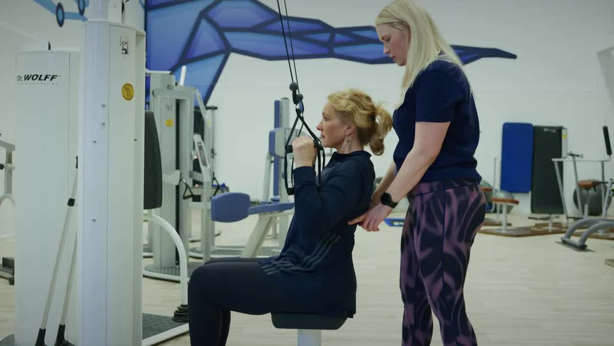 Physiotherapeutin begleitet eine Patientin beim Training an einem medizinischen Zuggerät