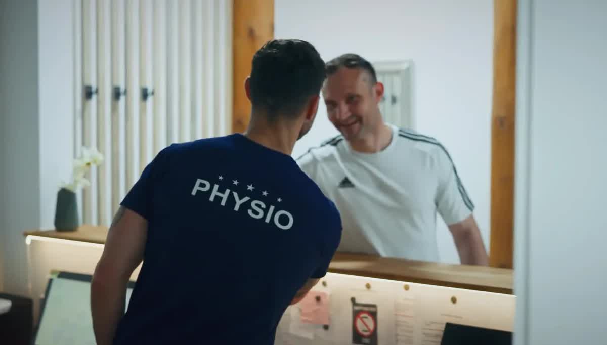 Physiotherapeut der POM MED begrüßt einen lächelnden Patienten an der Theke